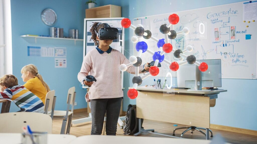 One student uses a virtual reality headset to explore an immersive 3D learning experience while other students sit nearby working on classroom tasks as they wait their turn to use the limited AR/VR kits.